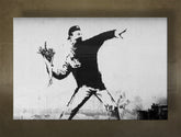 A fekete-fehér Banksy virágdobó fiú motívumot ábrázoló vászonkép látható, látható fakerettel, Papilora.